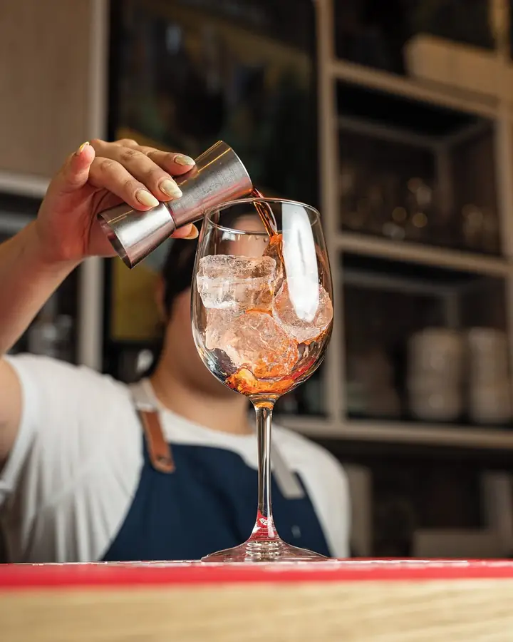 Bartender pouring a cocktail into a wine glass with ice