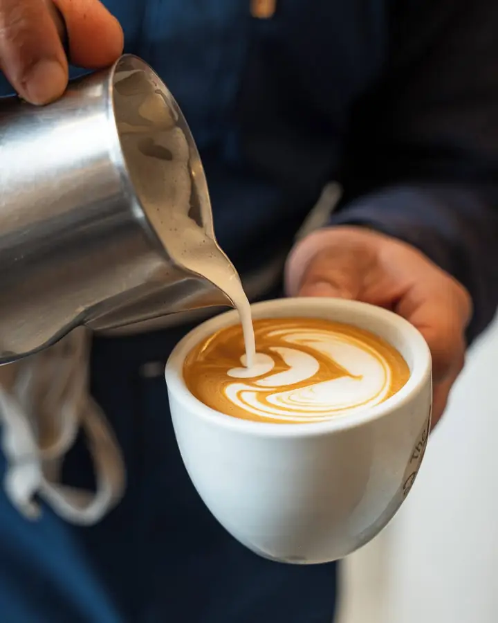 Barista pouring latte art into a white cup